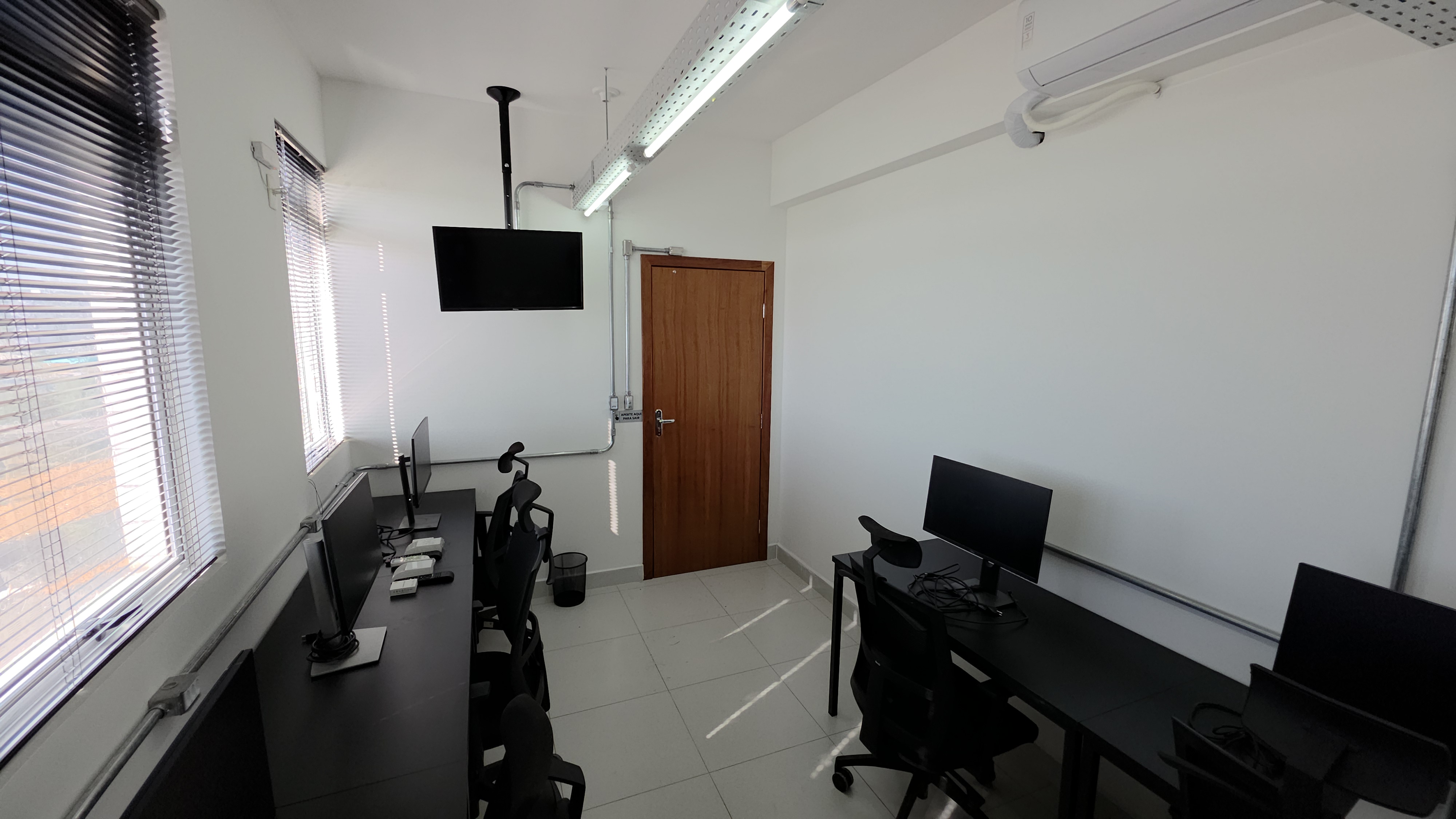 Sala privativa ampla com mesas, monitores e luz natural no Inconfidência em Betim